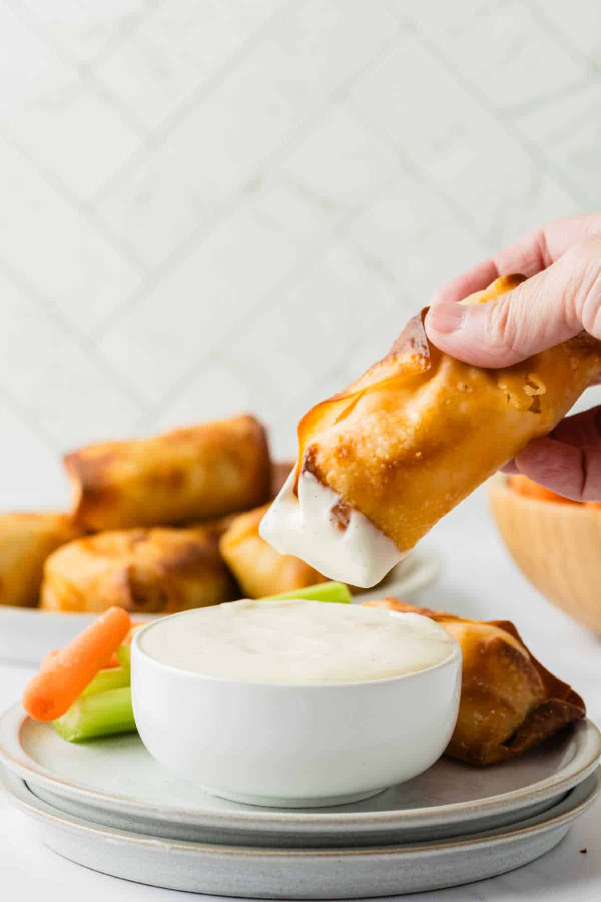 A hand dipping a buffalo chicken egg roll in ranch dressing.