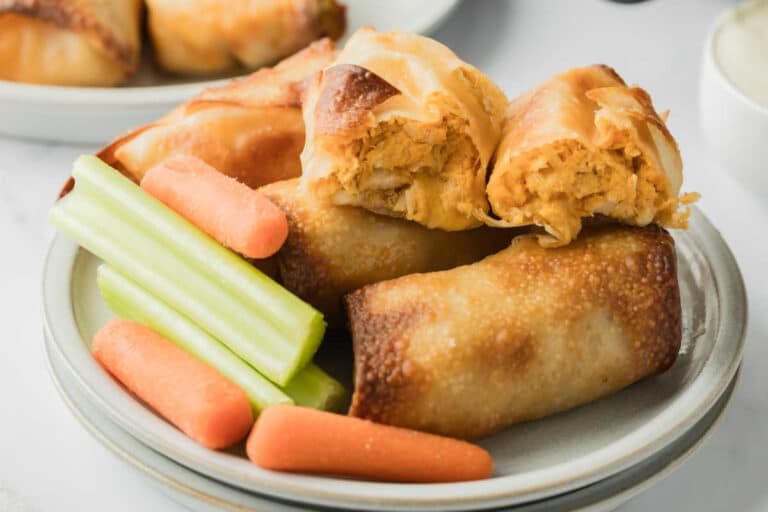 Air fryer buffalo chicken egg rolls on a plate with celery and carrot sticks.