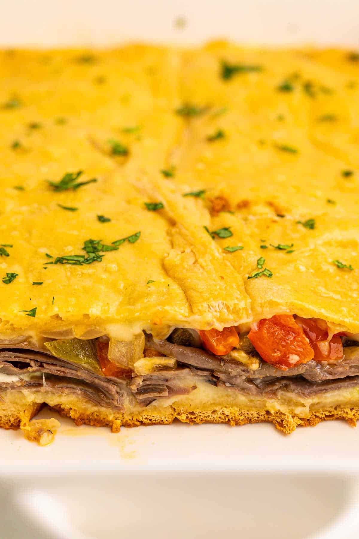 Philly cheesesteak squares in a pan with slices cut out.