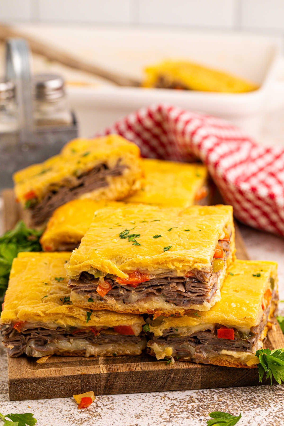 Philly cheesesteak squares on a wooden cutting board.