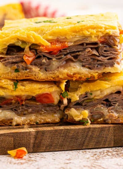 Philly cheesesteak squares on a wooden cutting board.