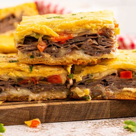 Philly cheesesteak squares on a wooden cutting board.