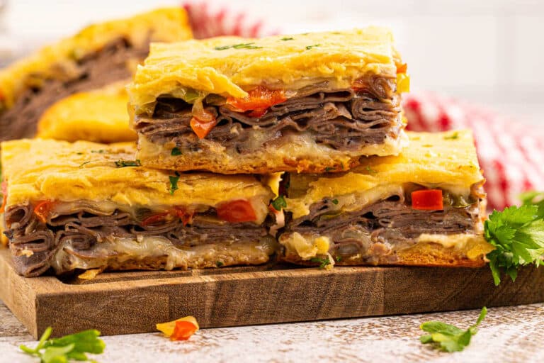 Philly cheesesteak squares on a wooden cutting board.