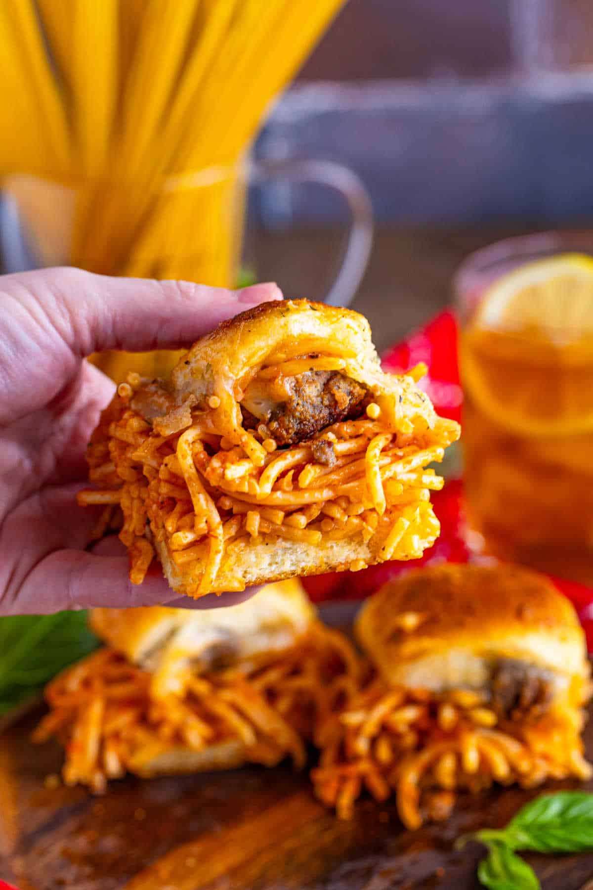 A hand holding a spaghetti and meatball slider.