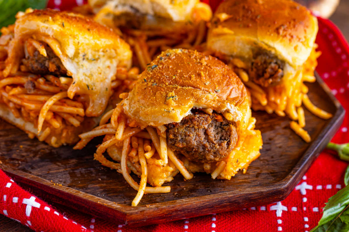 Spaghetti and meatball sliders on a wooden platter.