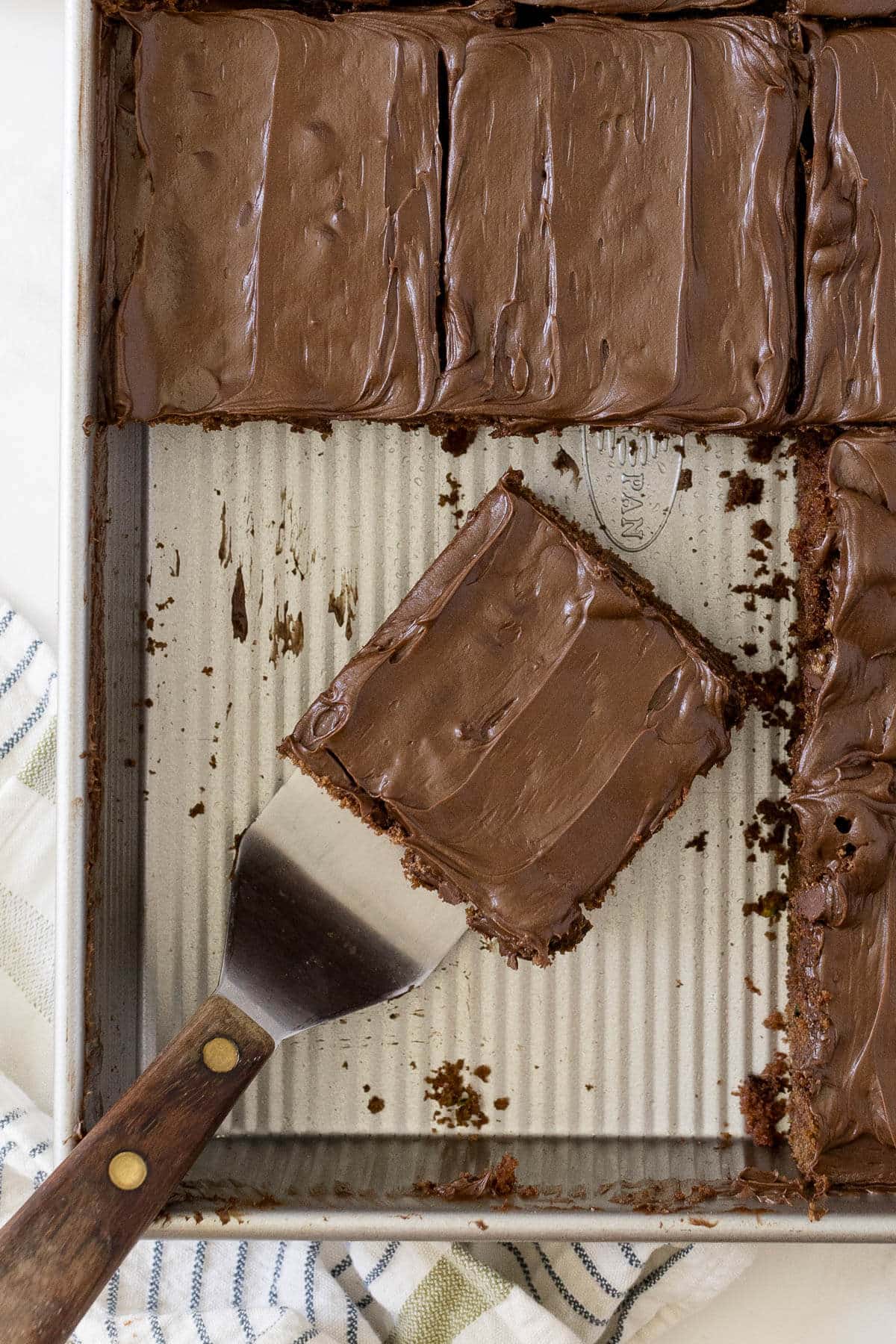 Chocolate zucchini cake cut into slices in a pan with a spatula.