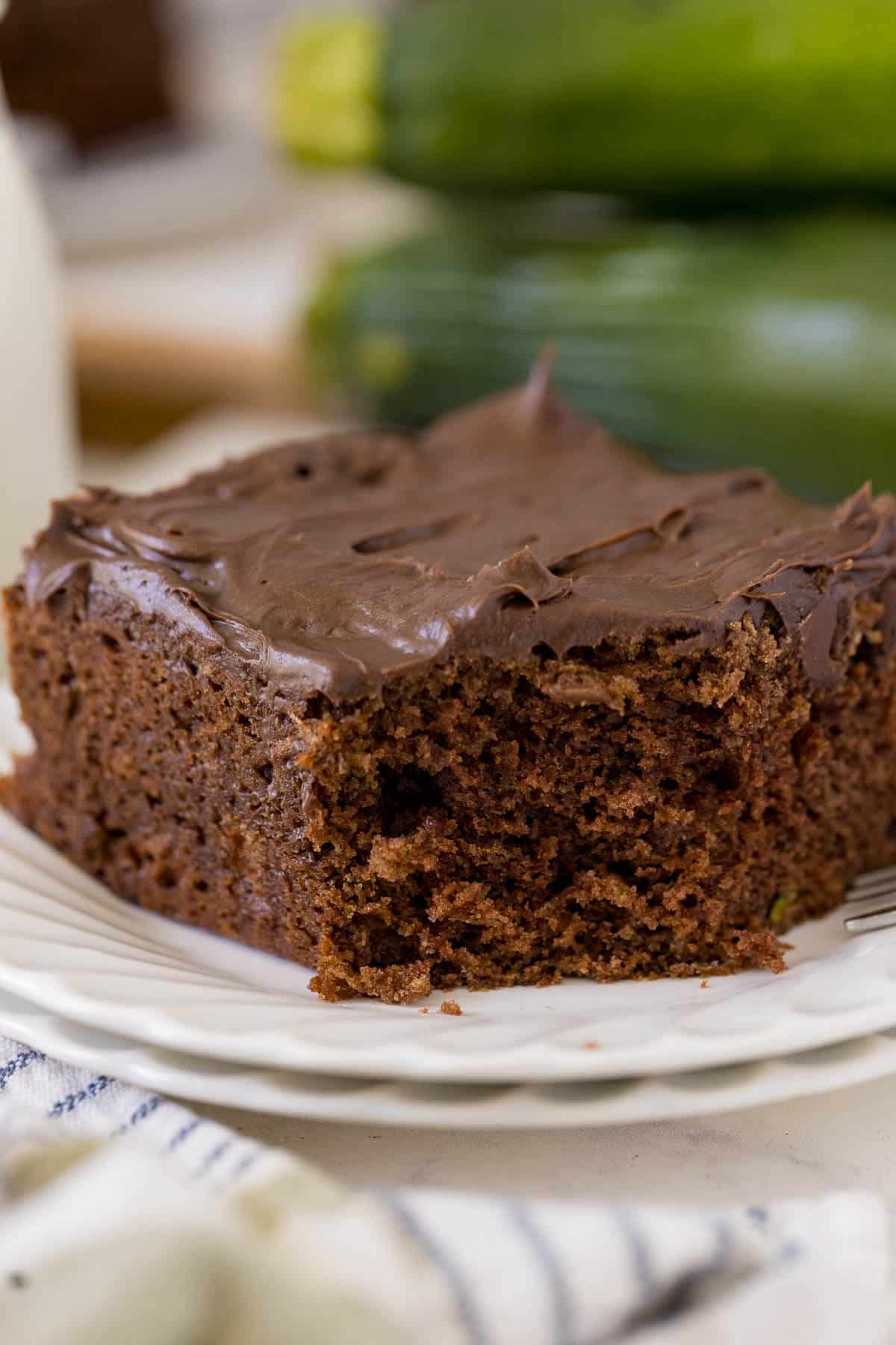 A slice of chocolate zucchini cake on a plate with a bite out of it.