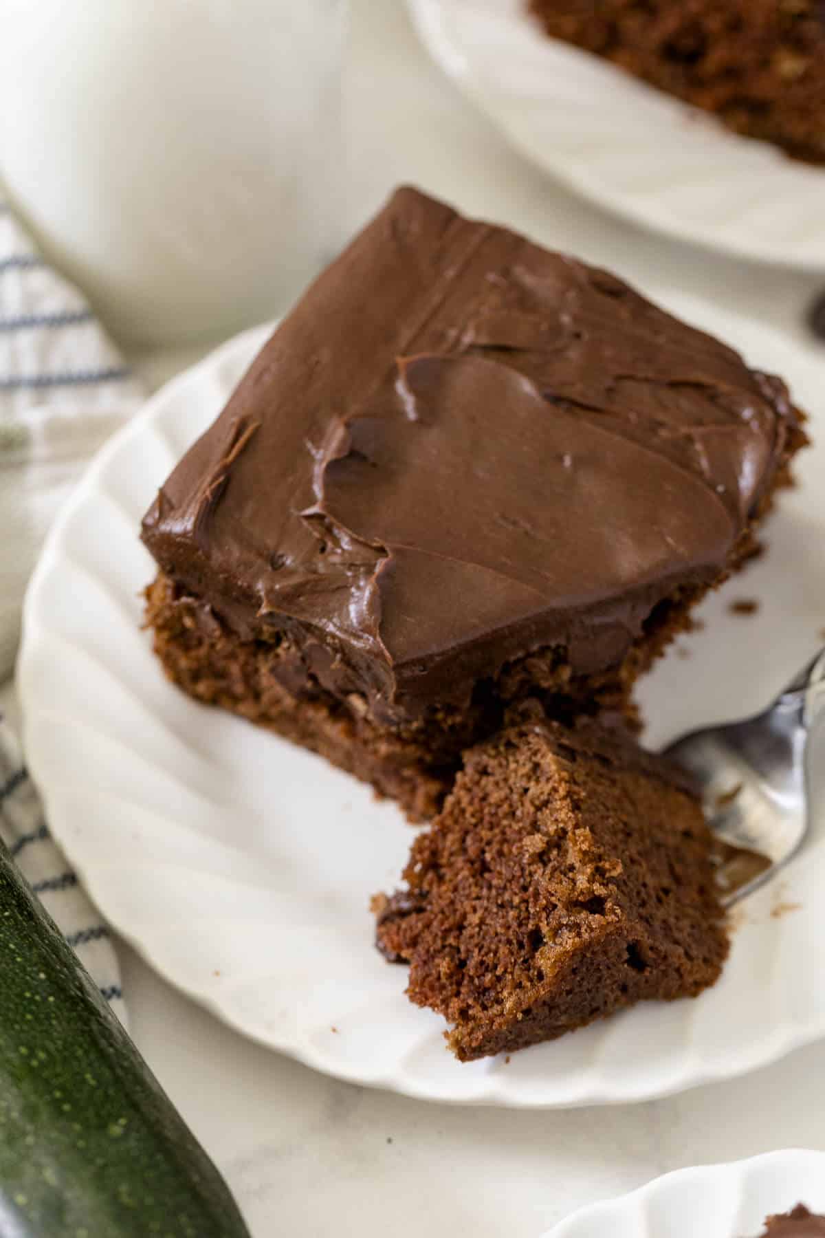 A piece of chocolate zucchini cake on a plate with a bite on a fork.