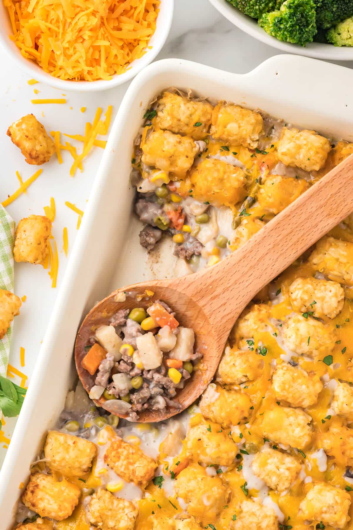 The recipe with a wooden spoon in a dish with some casserole scooped out.