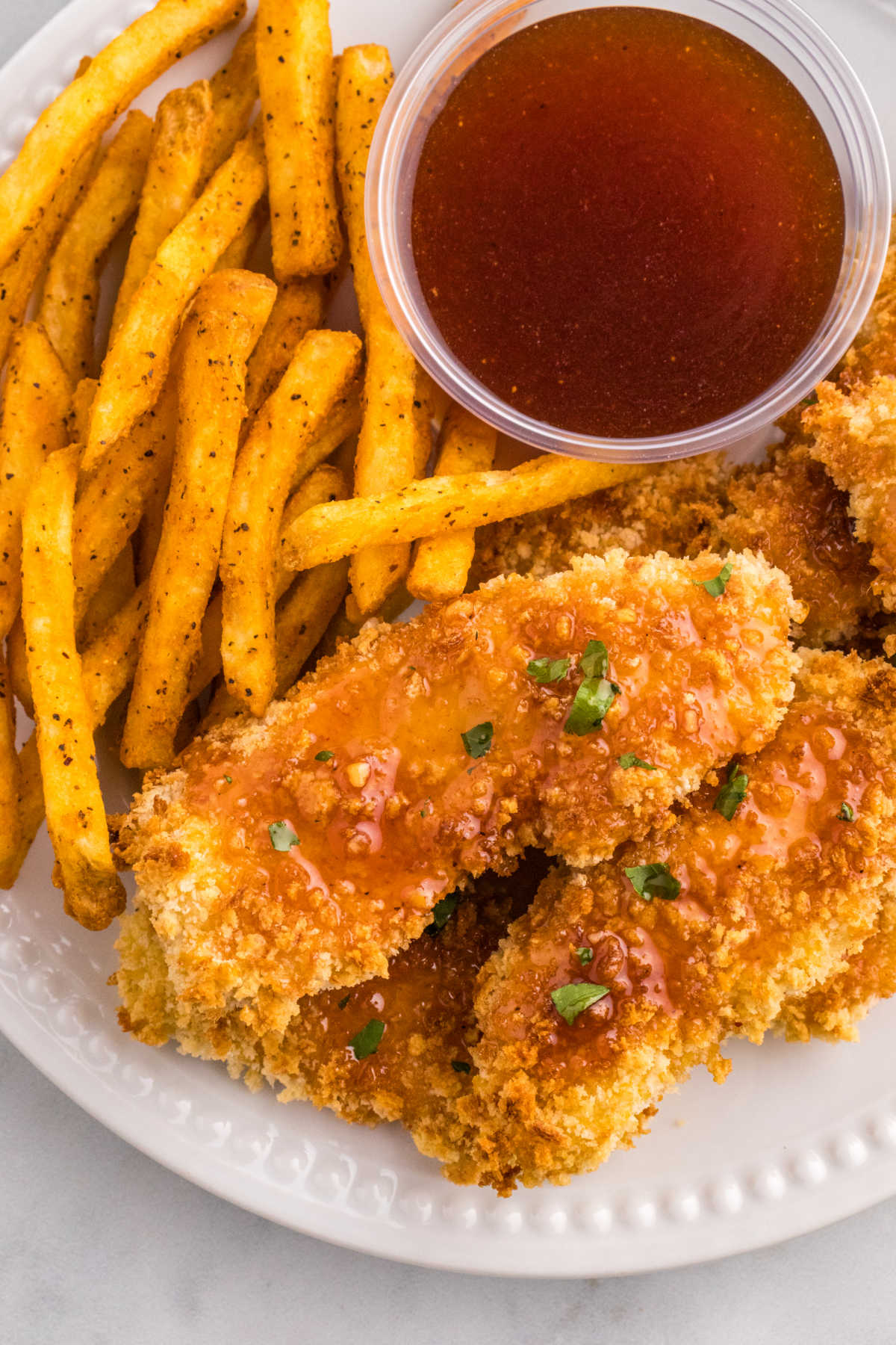 Hot honey chicken tenders on a plate with fries and hot honey sauce.