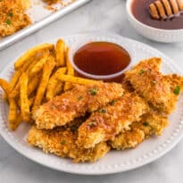 Hot honey chicken tenders on a plate with fries and hot honey sauce.