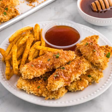 Hot honey chicken tenders on a plate with fries and hot honey sauce.