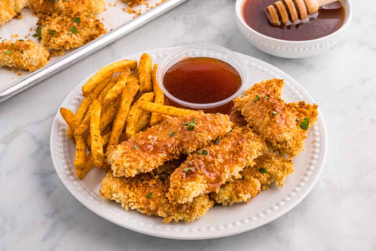 Hot honey chicken tenders on a plate with fries and hot honey sauce.