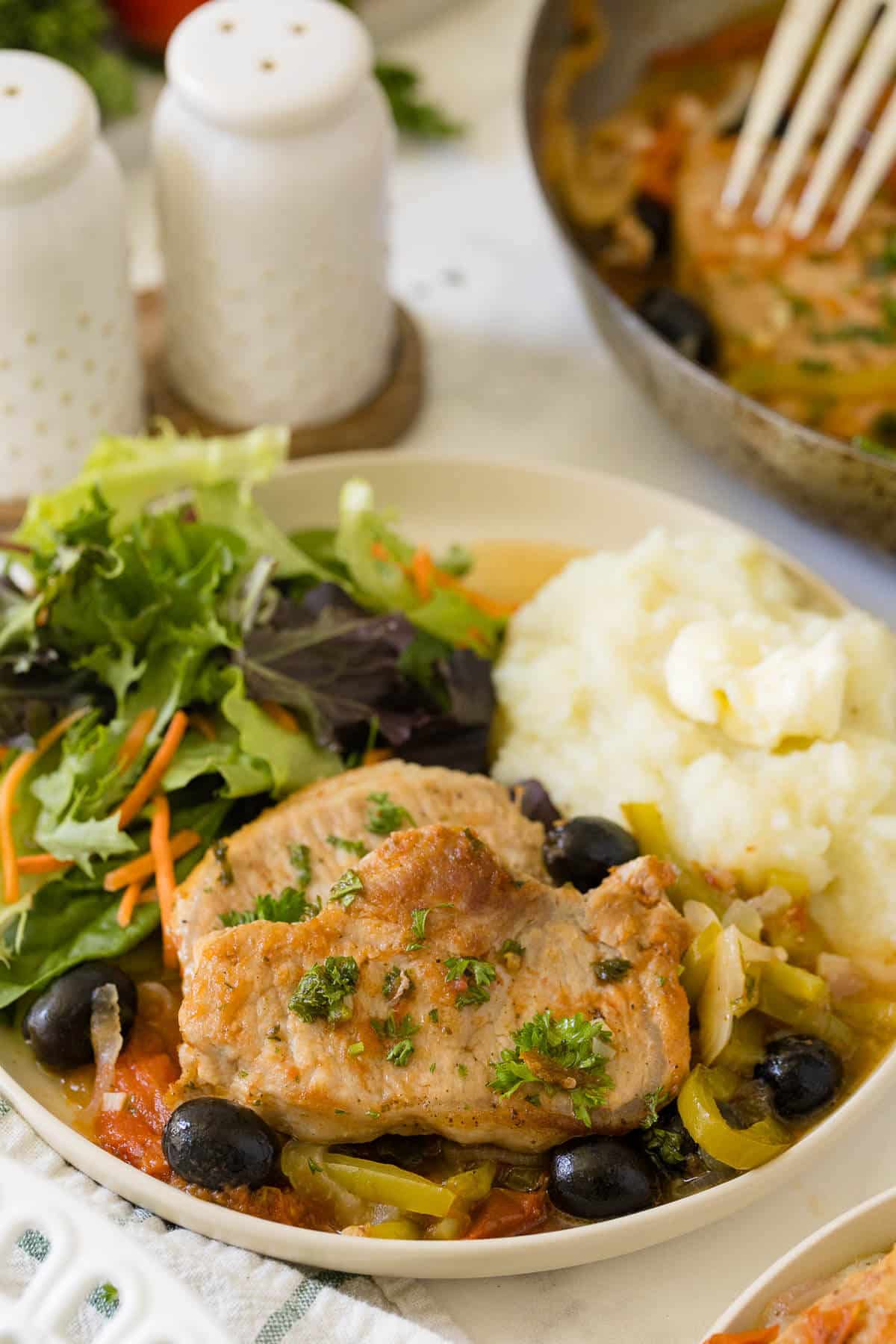 Savory pork chops on a plate with salad and mashed potatoes.
