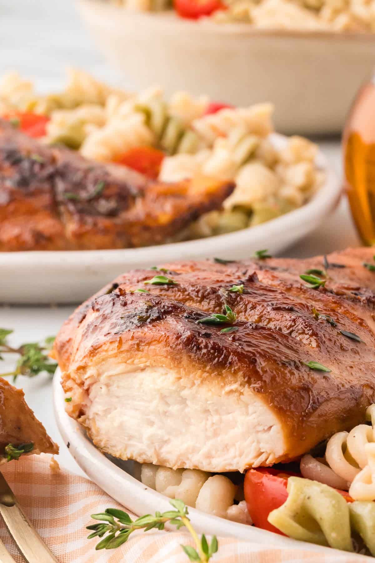 Sliced chicken breast on top of pasta salad on a plate.