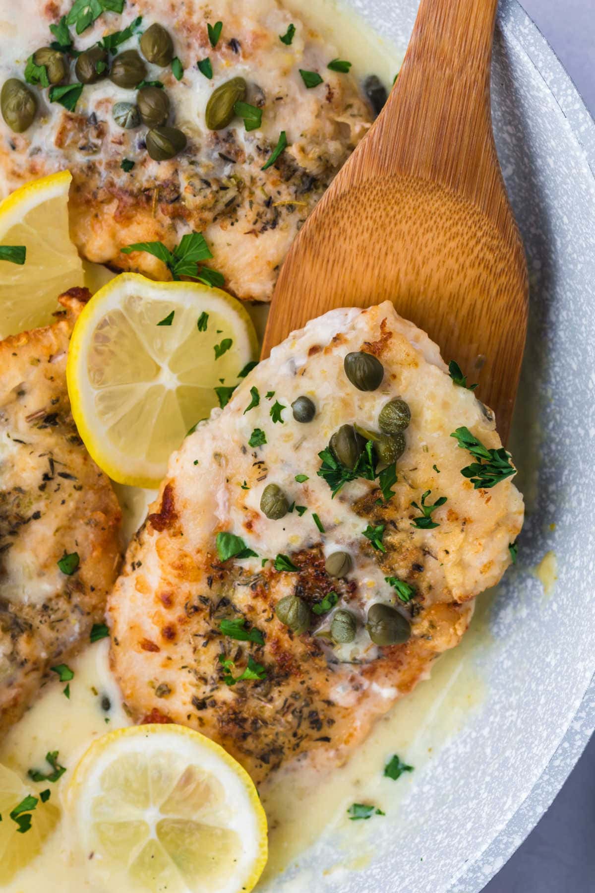 A chicken breast on a wooden spoon in a pan.