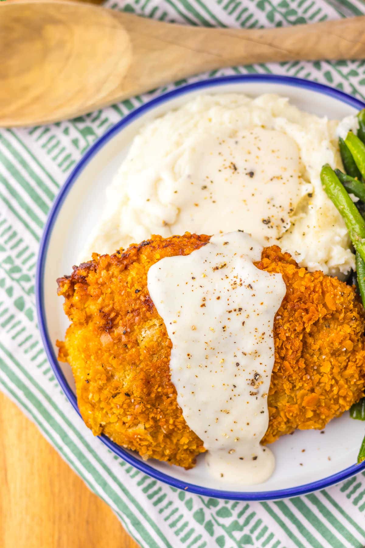 A plate with the recipe on a plate with mashed potatoes and green beans.