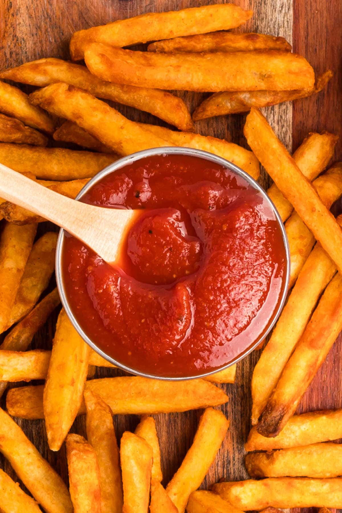 The recipe in a container with a wooden spoon surrounded by fries.
