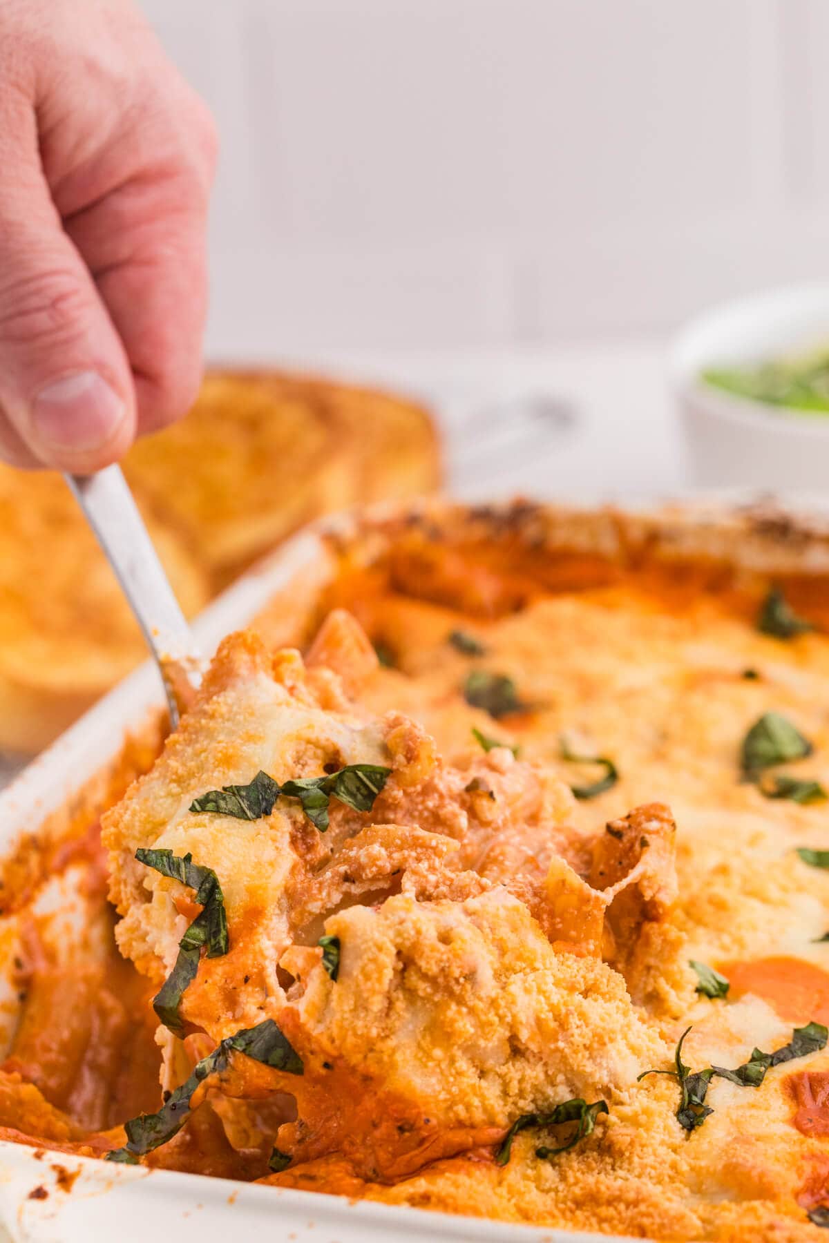 A hand lifting a serving spoon with the recipe on it from a casserole dish.