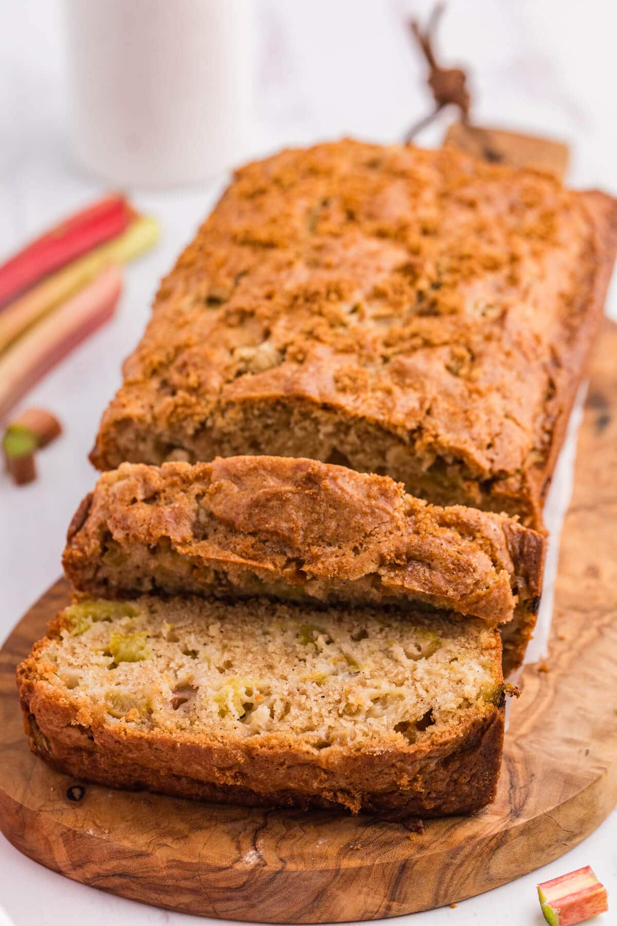 A loaf of rhubarb bread on a wooden cutting board with a couple slices cut off the end.