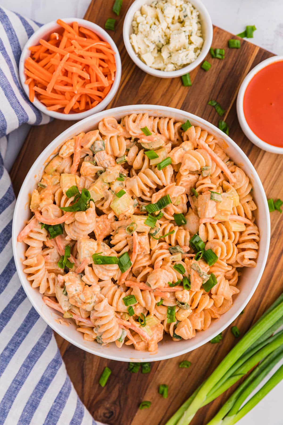 A bowl of Buffalo Chicken Pasta Salad on a wooden cutting board surrounded by ingredients.