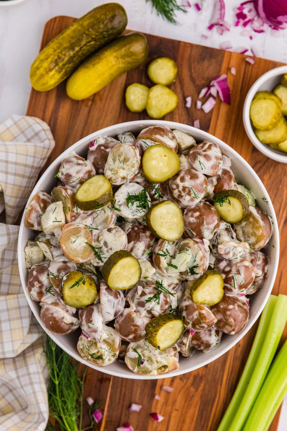 A bowl of dill pickle potato salad on a wooden cutting board.