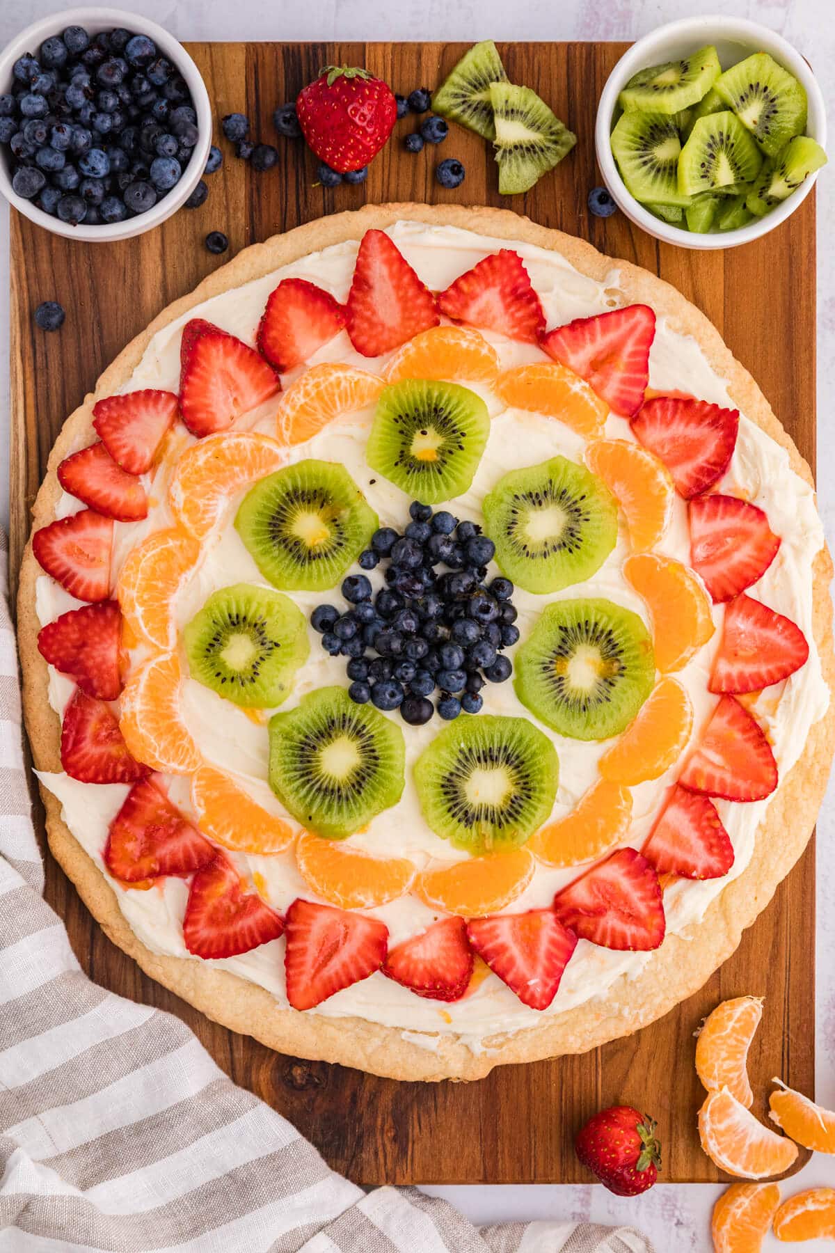 Fruit pizza on a wooden surface surrounded by fruit.