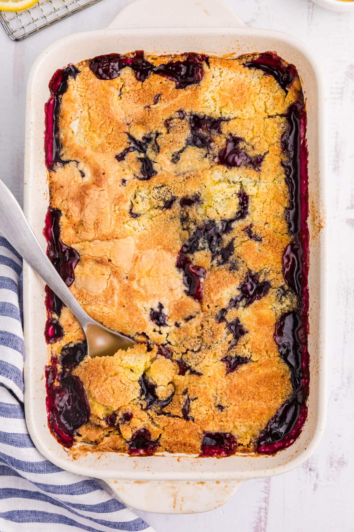 Lemon blueberry dump cake in a pan on a white surface.