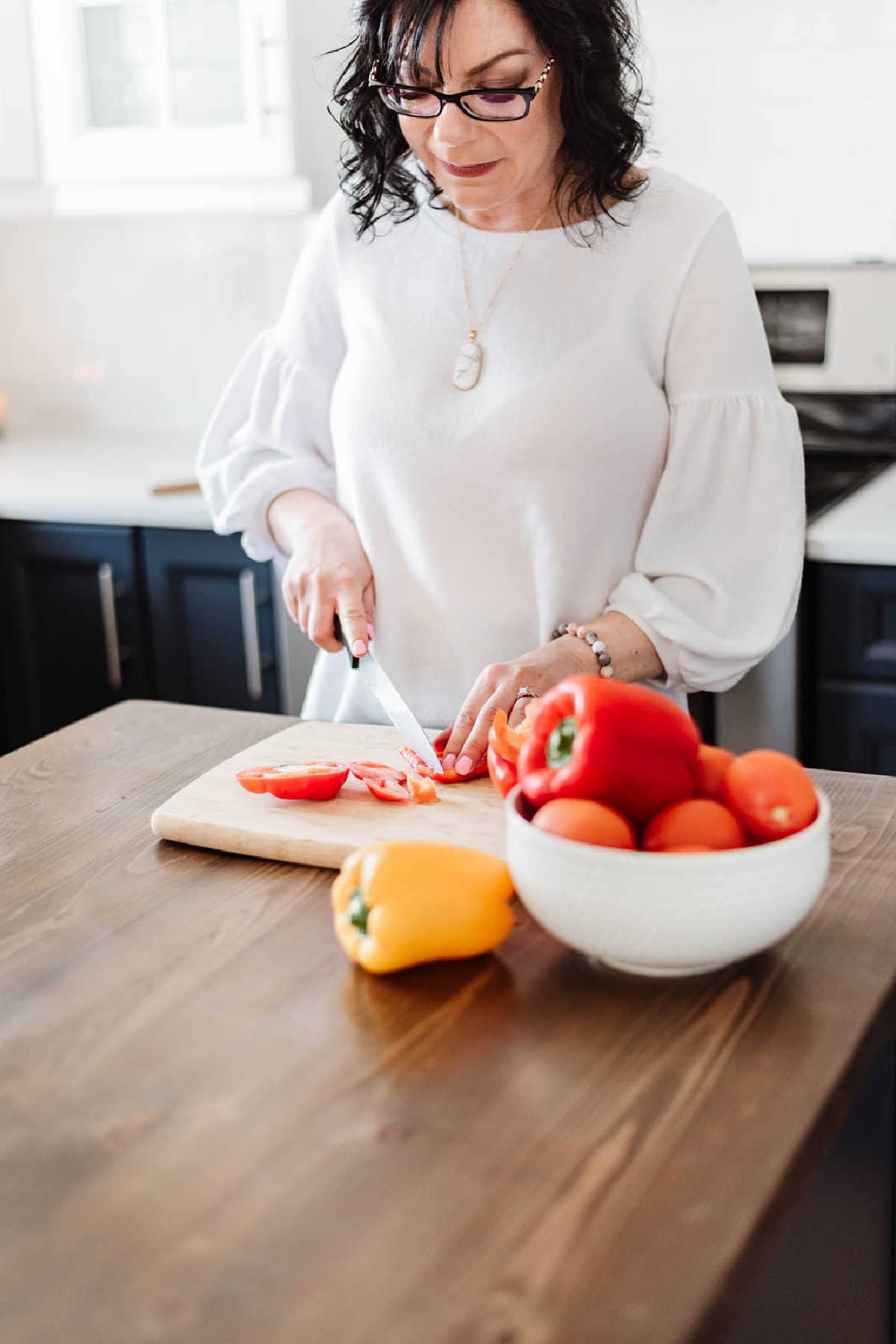 A woman in a kitchen cutting a red pepper.
