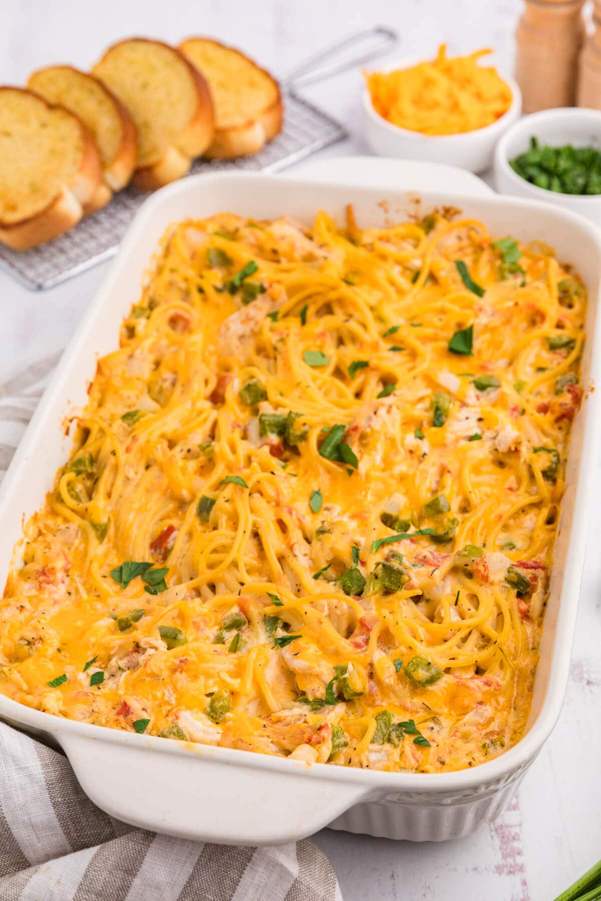 Creamy chicken spaghetti in a casserole dish with garlic bread slices in the background.