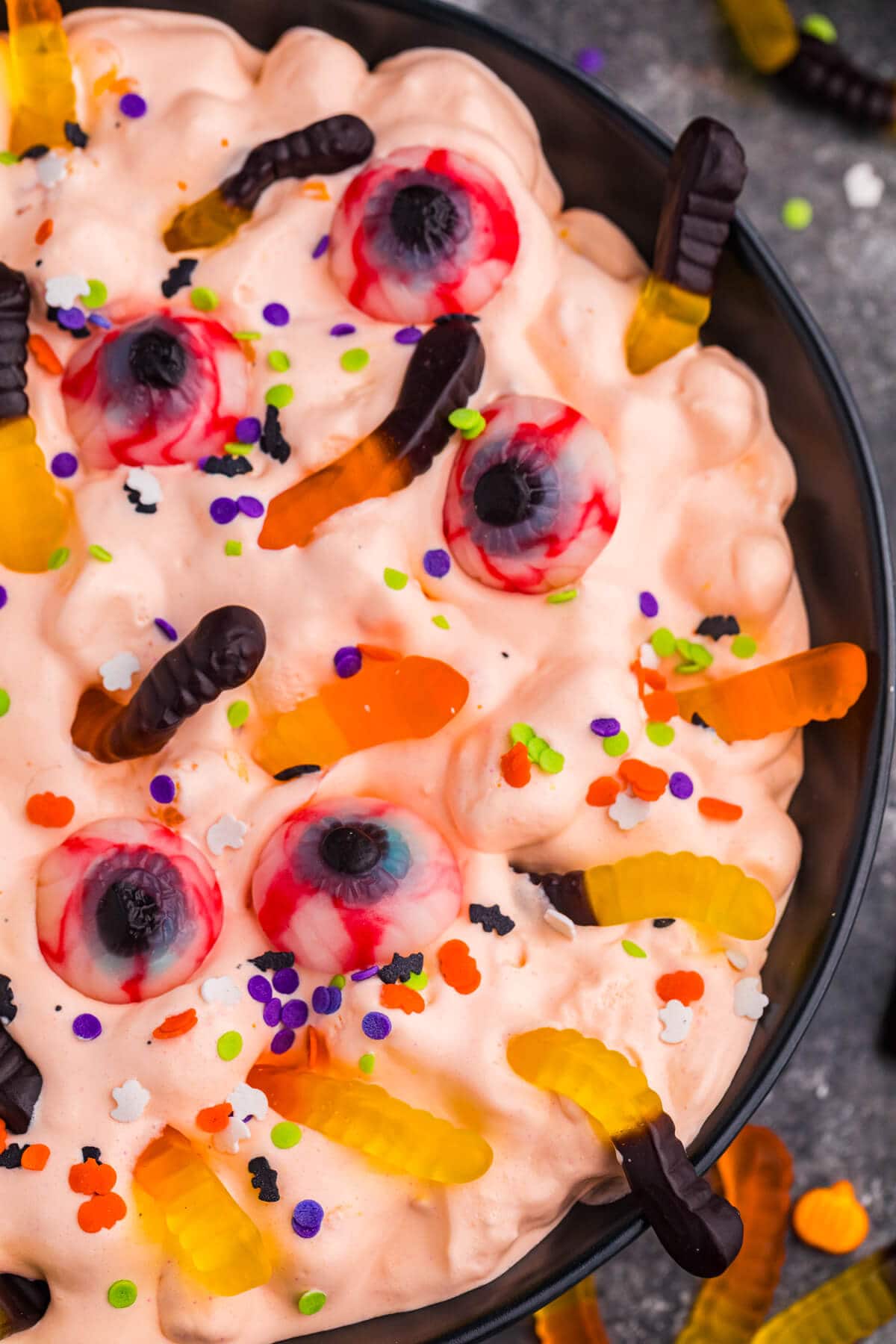 Close-up detail of orange fluff topped with gummy worms, candy eyeballs, and colorful Halloween sprinkles.