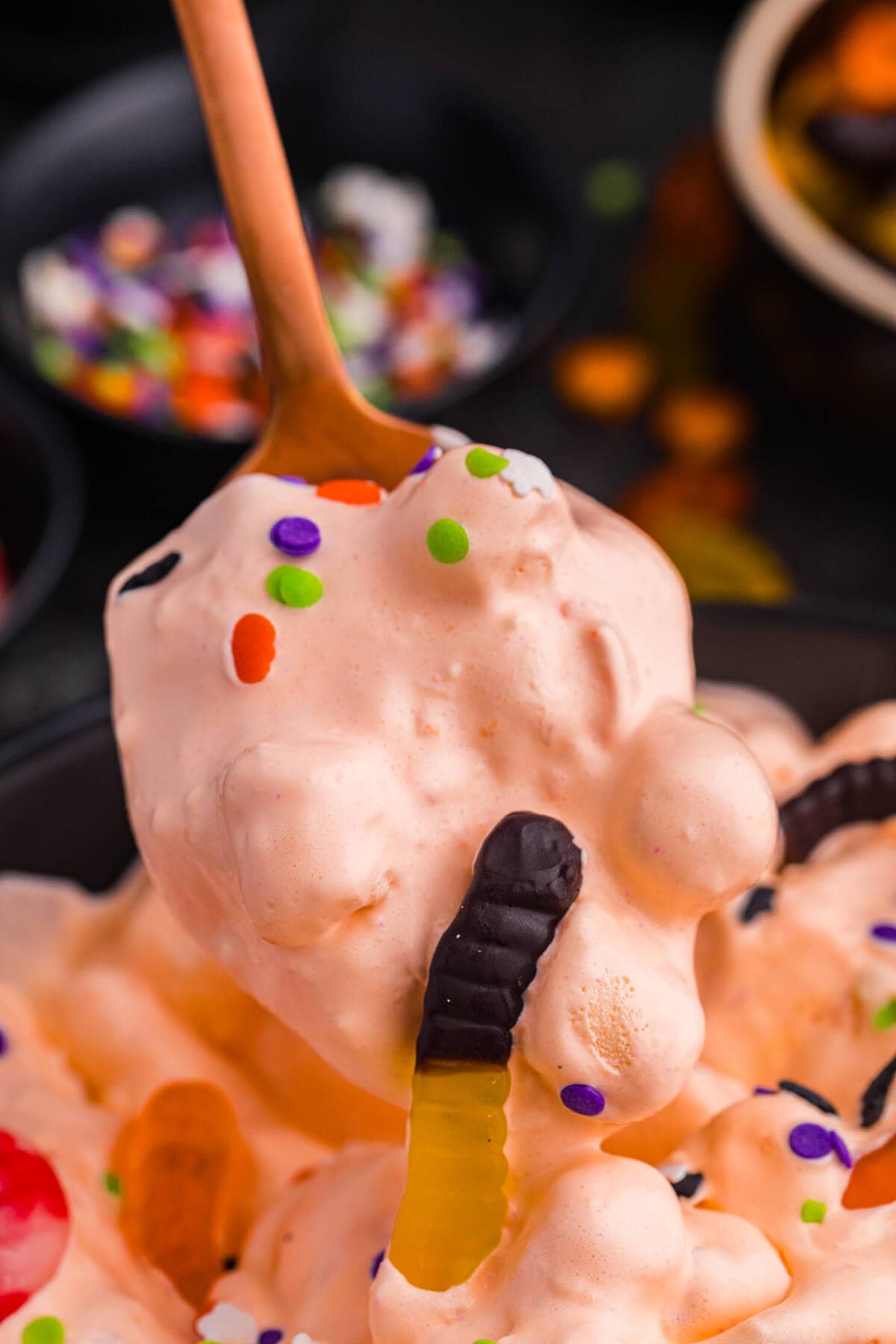 Spoon lifting a scoop of the recipe, showing fluffy texture with marshmallows, gummy worms, and sprinkles.