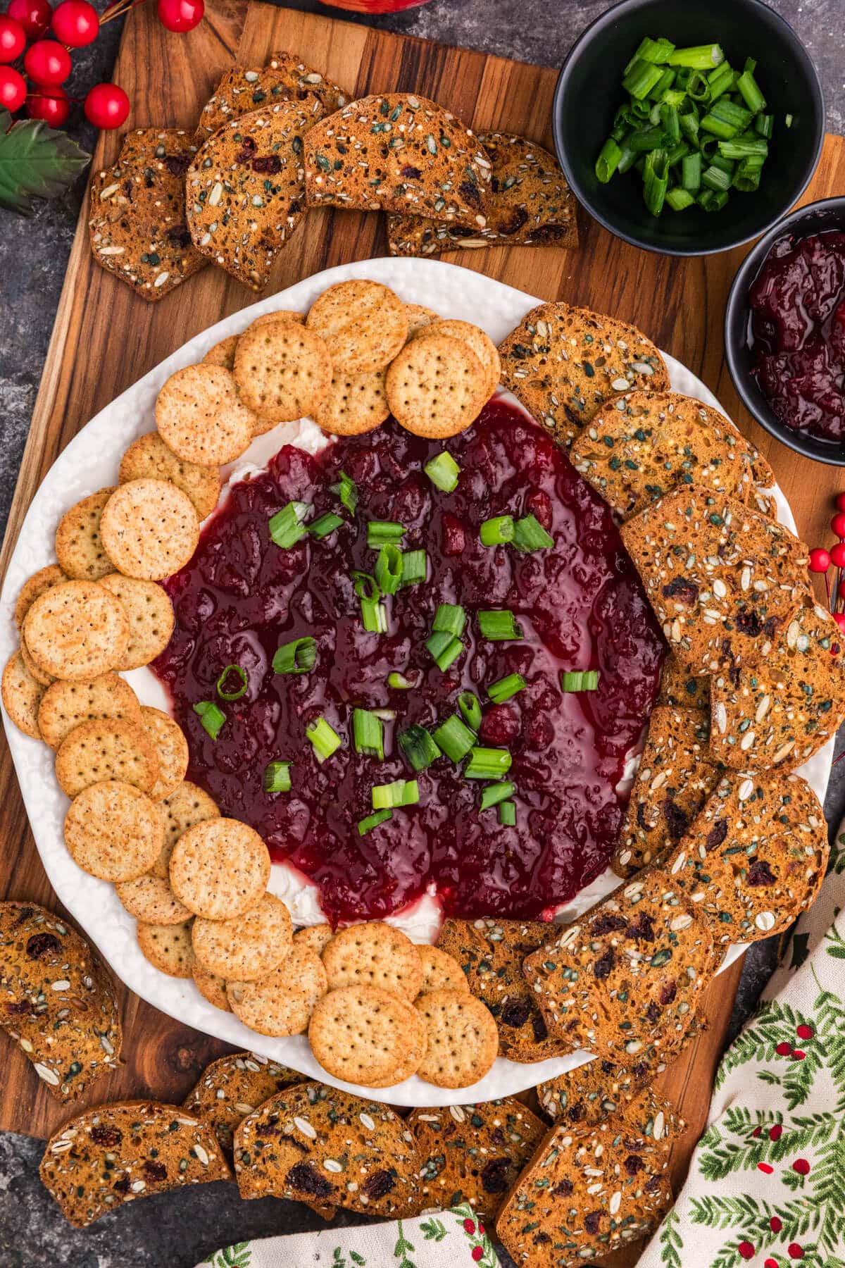 Cranberry Cream Cheese Dip on a round platter topped with dark red cranberry sauce and chopped green onions, surrounded by round and seeded crackers.