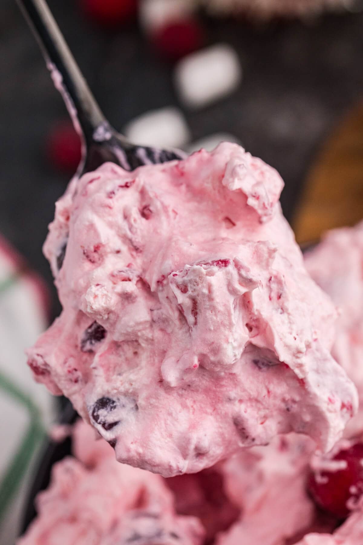 Close-up of a spoonful of fluffy pink dessert with visible chunks of berries and marshmallows, showcasing its creamy texture and festive ingredients.