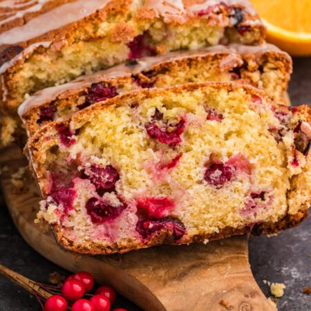 A loaf of cranberry orange bread garnished with bright orange slices, highlighting its fruity flavor and texture.