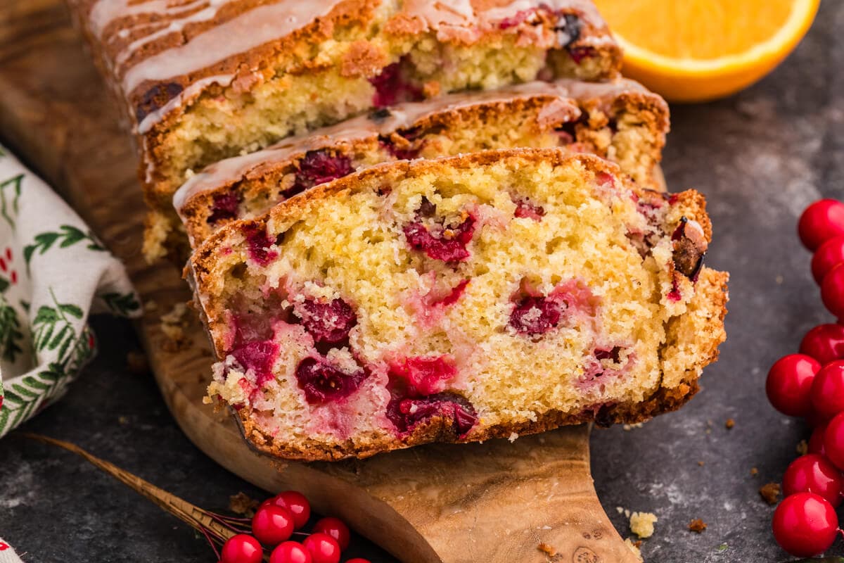 A loaf of cranberry orange bread garnished with bright orange slices, highlighting its fruity flavor and texture.