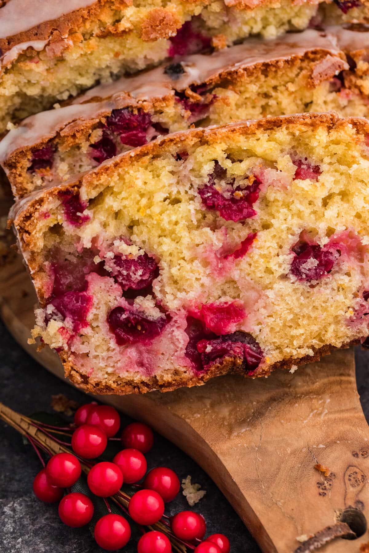 A loaf of cranberry bread, partially sliced to show its rich color and texture, with a piece removed from the side.