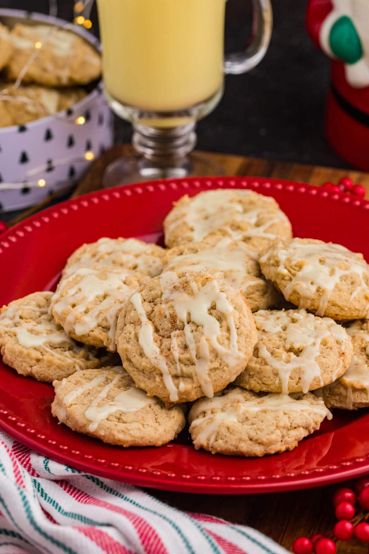 A plate of eggnog cookies beside a glass of milk, with a decorated Christmas tree in the background.