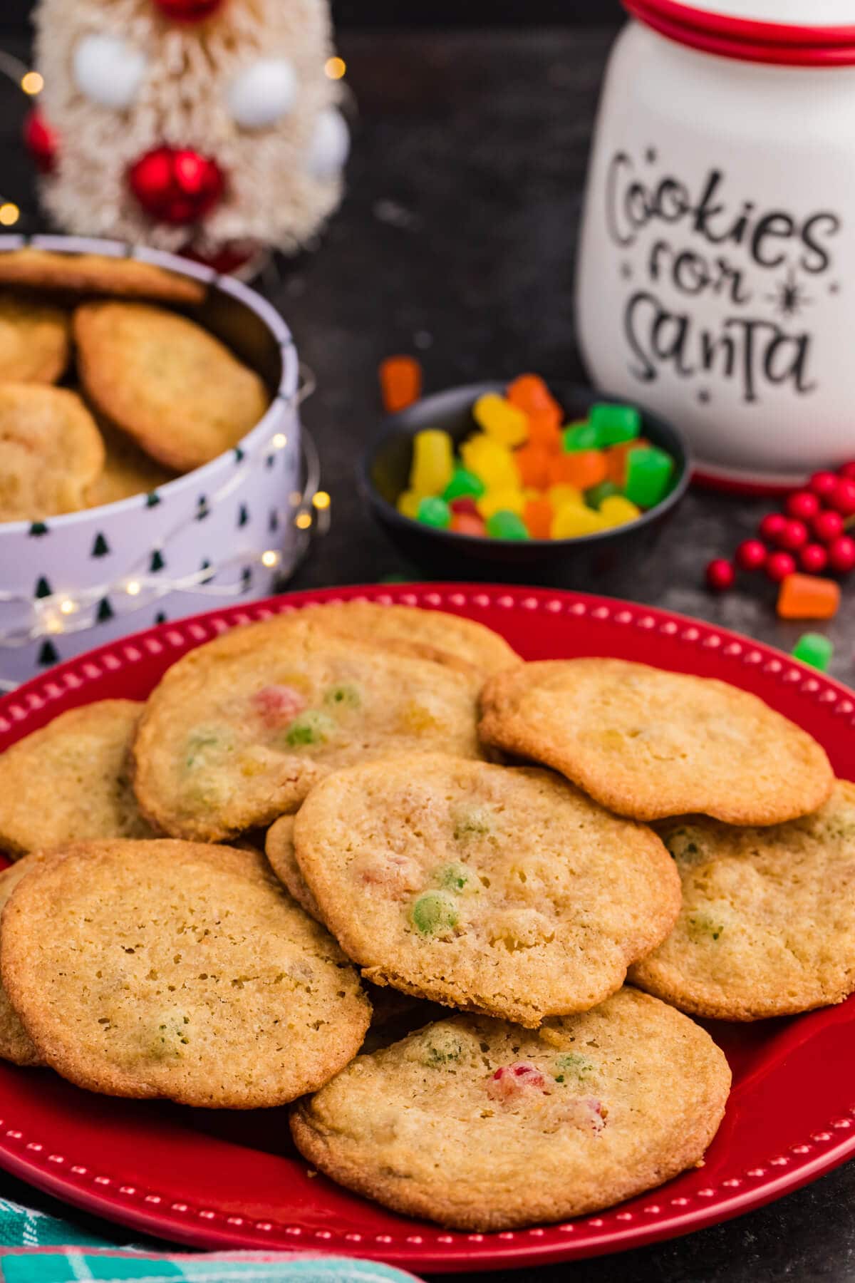 Gumdrop cookies on a red plate, studded with colorful candy pieces, surrounded by festive Christmas decor and a &ldquo;Cookies for Santa&rdquo; jar.