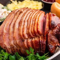 Juicy brown sugar ham, spiral-sliced and glazed to perfection, served on a white platter with fresh parsley garnish.