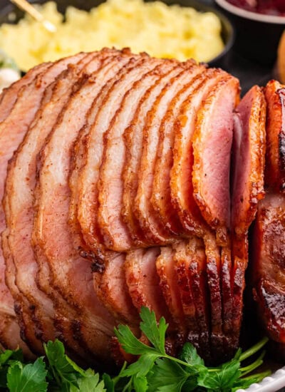 Juicy brown sugar ham, spiral-sliced and glazed to perfection, served on a white platter with fresh parsley garnish.