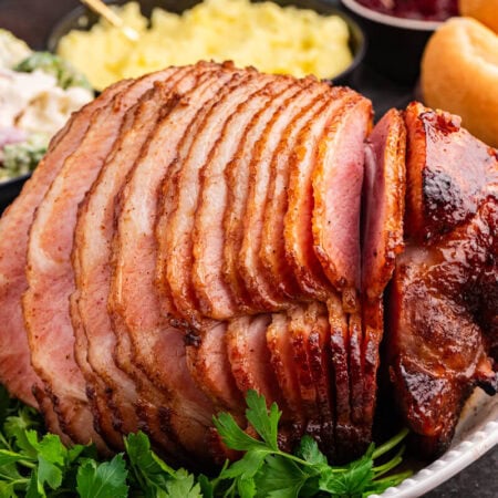 Juicy brown sugar ham, spiral-sliced and glazed to perfection, served on a white platter with fresh parsley garnish.