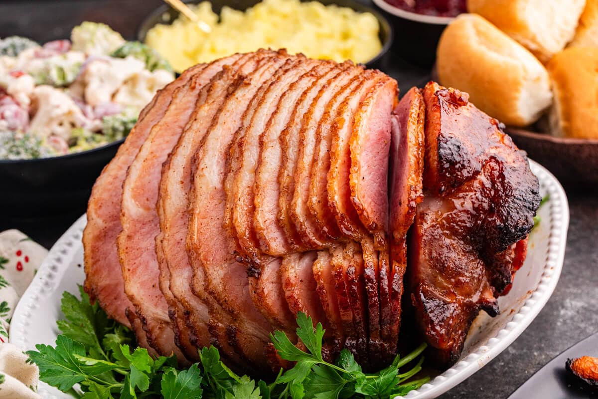 Juicy brown sugar ham, spiral-sliced and glazed to perfection, served on a white platter with fresh parsley garnish.
