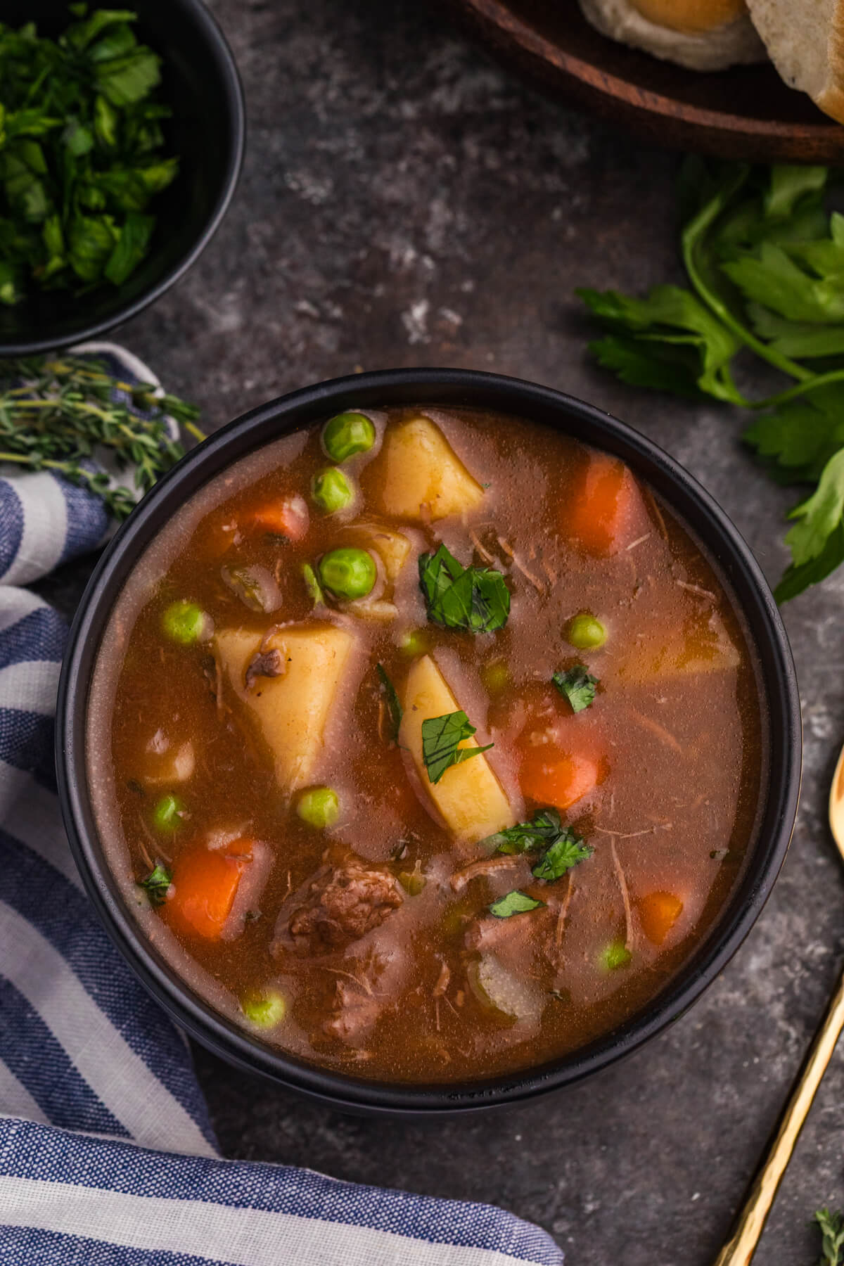 Top view of rustic meat and vegetable soup with potatoes, carrots, peas, and shredded beef in a black bowl.
