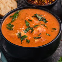 Creamy tortellini soup in black bowl with fresh basil garnish.