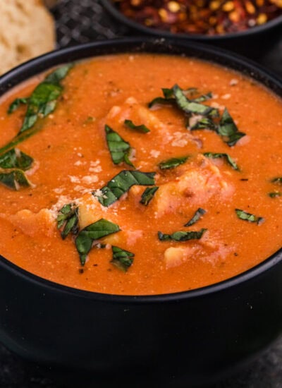 Creamy tortellini soup in black bowl with fresh basil garnish.
