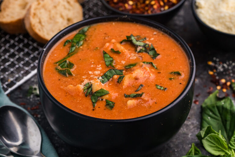 Creamy tortellini soup in black bowl with fresh basil garnish.