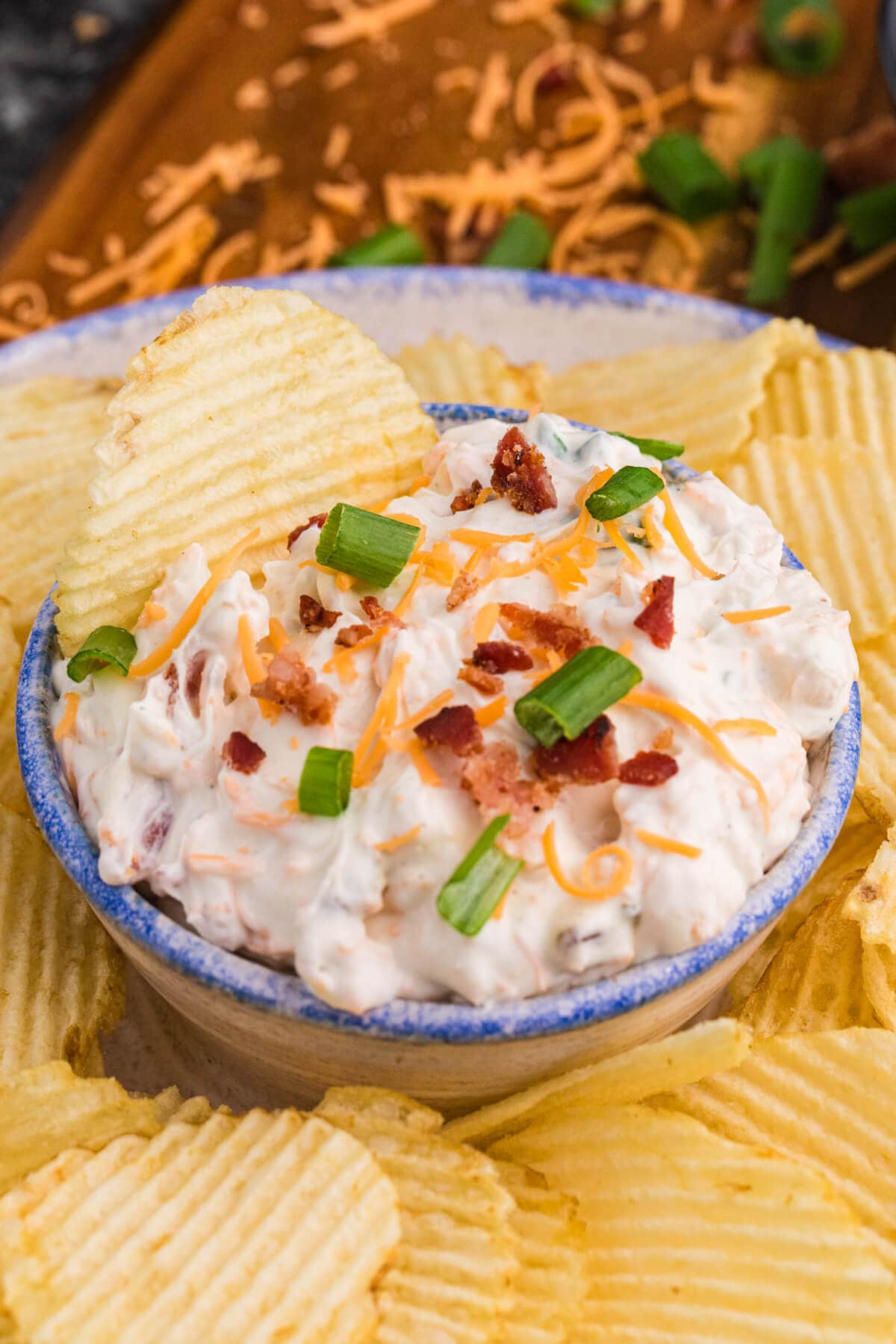 Close-up of loaded bacon cheddar dip with green onions and potato chips.