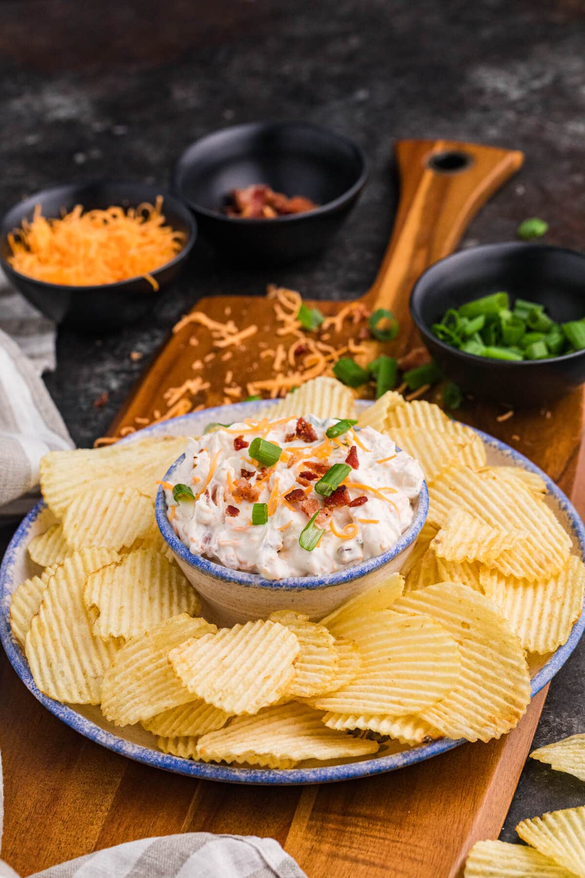 Creamy bacon cheddar ranch dip garnished with green onions, surrounded by ridged potato chips.