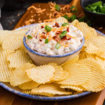 Close-up of loaded bacon cheddar dip with green onions and potato chips.